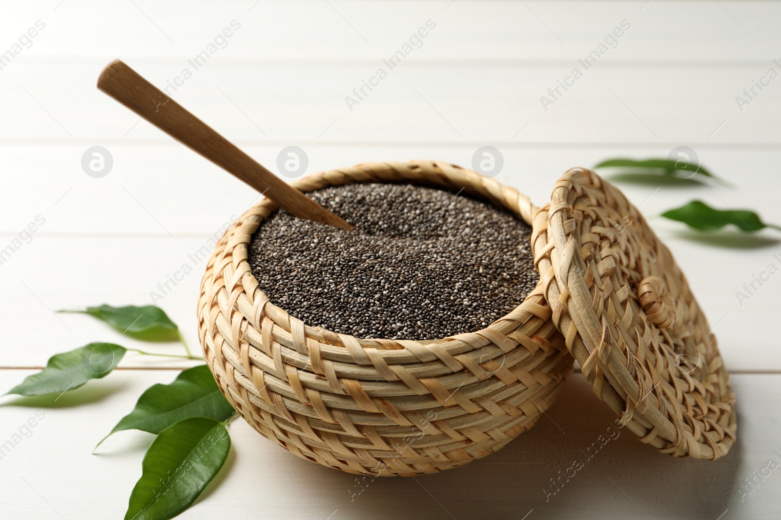 Photo of Wicker box with chia seeds and spoon on white wooden table