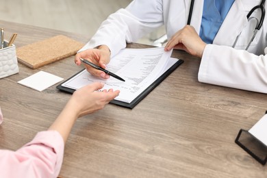 Doctor with results of laboratory test consulting pregnant patient in clinic, closeup