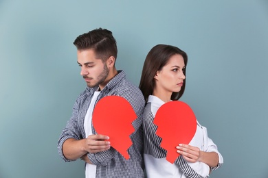 Young couple with torn paper heart on color background. Relationship problems