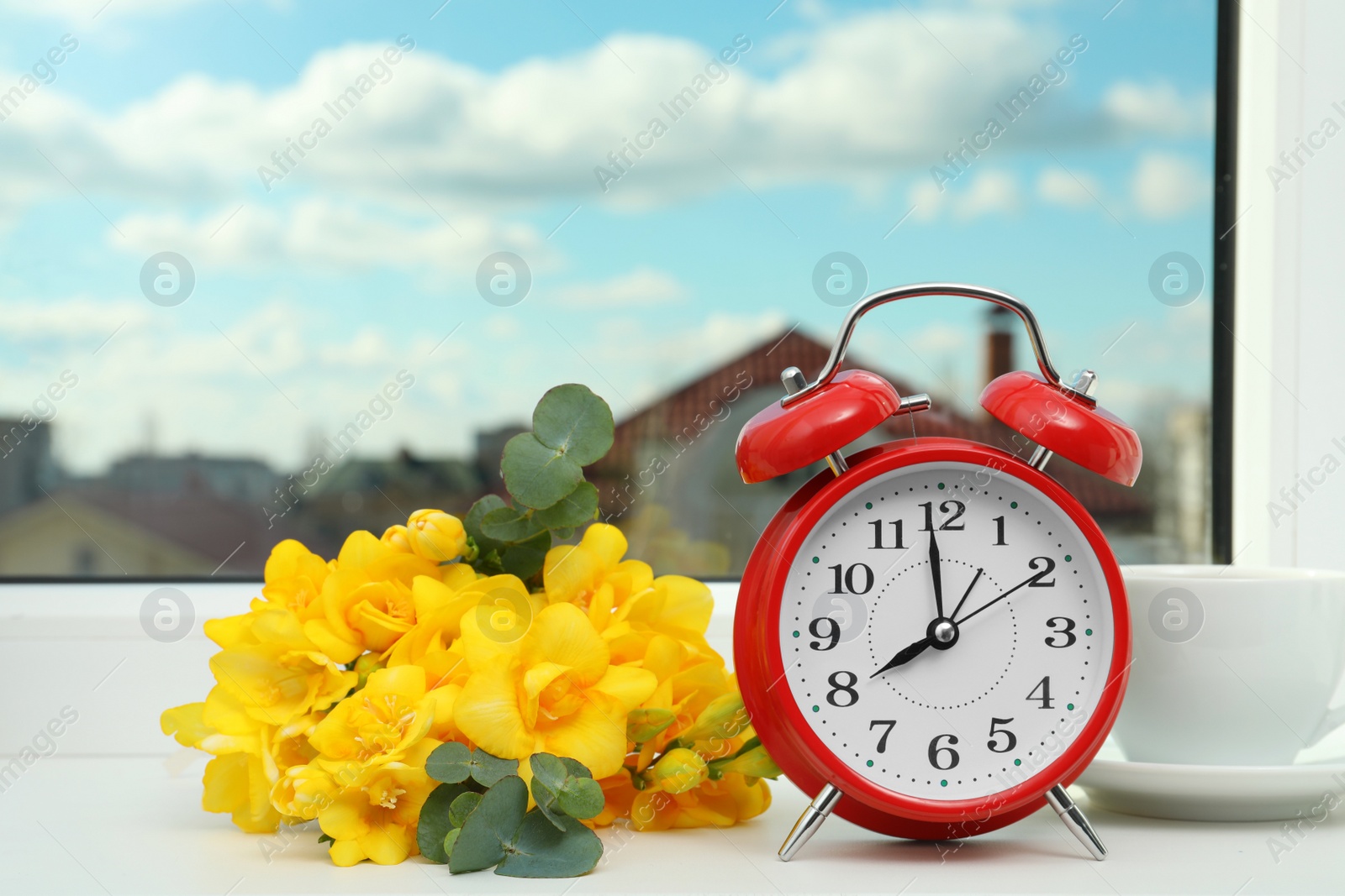 Photo of Alarm clock, beautiful yellow freesias and cup of drink on windowsill. Good morning