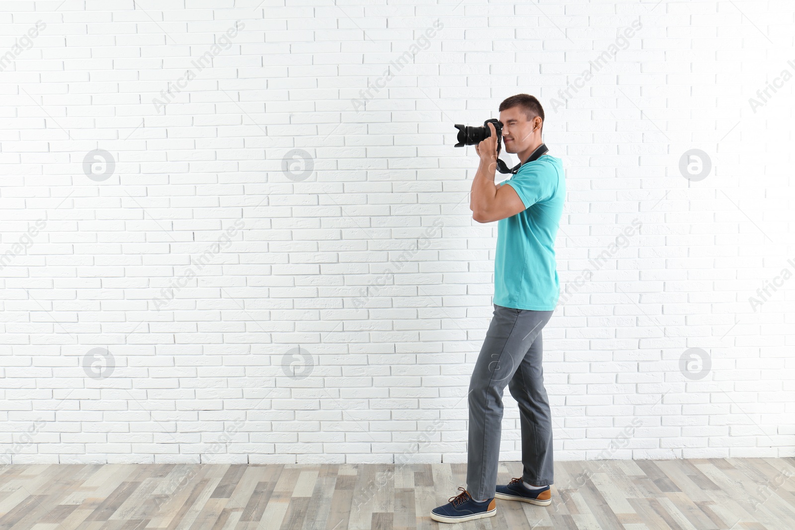 Photo of Young professional photographer taking picture near brick wall. Space for text