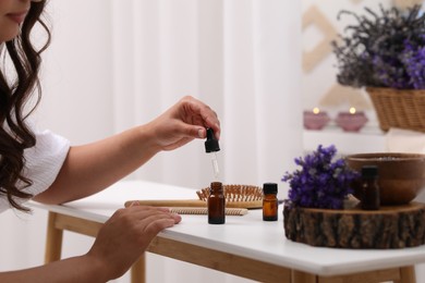 Woman with bottle of essential oil at table indoors, closeup