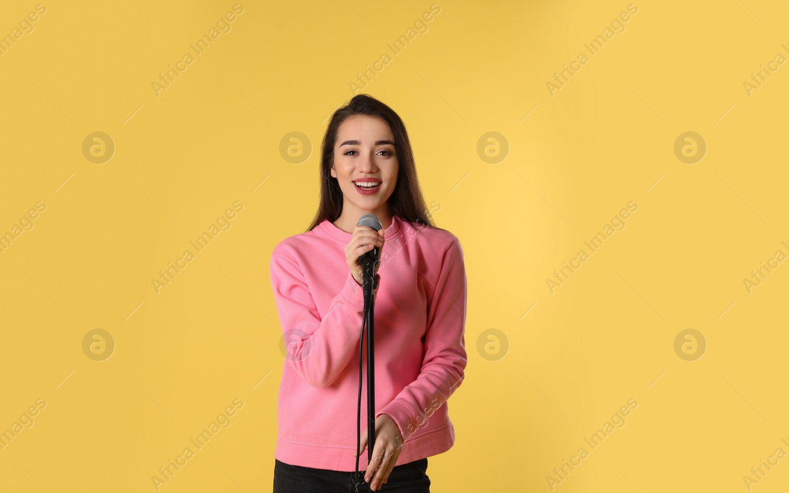 Photo of Young woman in casual clothes posing with microphone on color background. Space for text