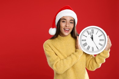 Photo of Woman in Santa hat with clock on red background, space for text. New Year countdown