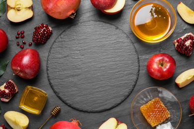 Photo of Frame of honey, apples and pomegranates on black table, flat lay with space for text. Rosh Hashanah holiday