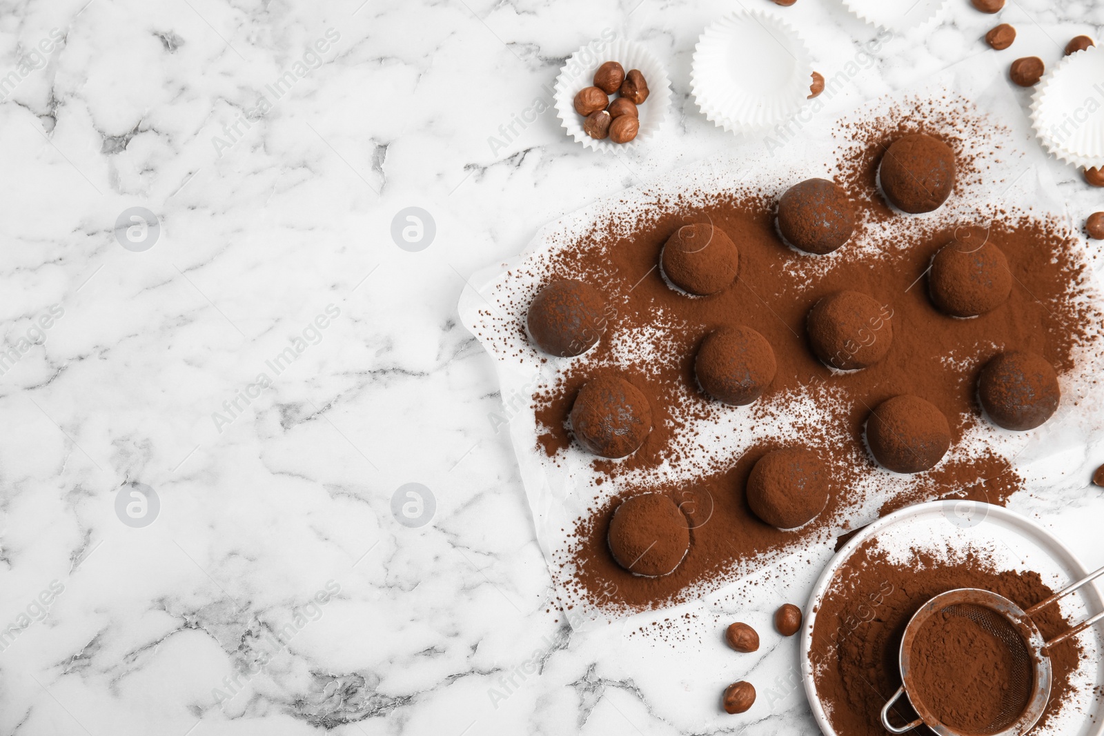 Photo of Delicious chocolate truffles with cocoa powder and hazelnuts on white marble table, flat lay. Space for text