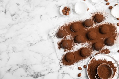 Delicious chocolate truffles with cocoa powder and hazelnuts on white marble table, flat lay. Space for text