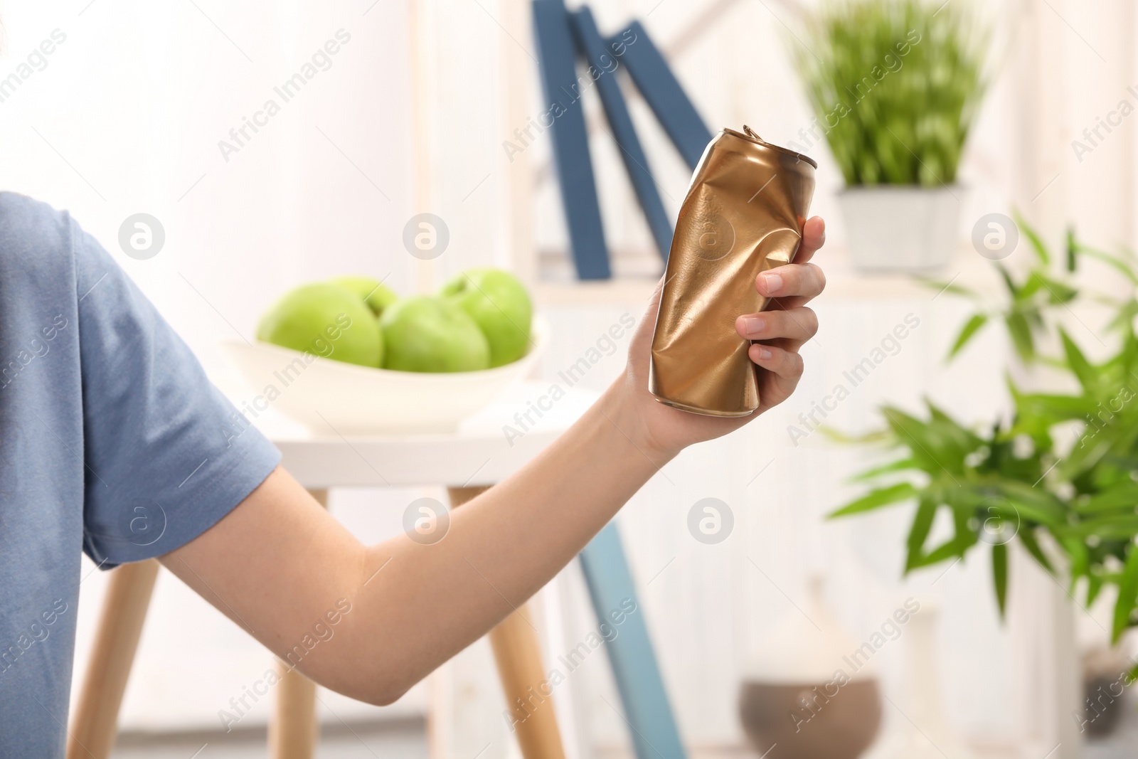 Photo of Woman holding crumpled aluminum can on blurred background. Metal waste recycling