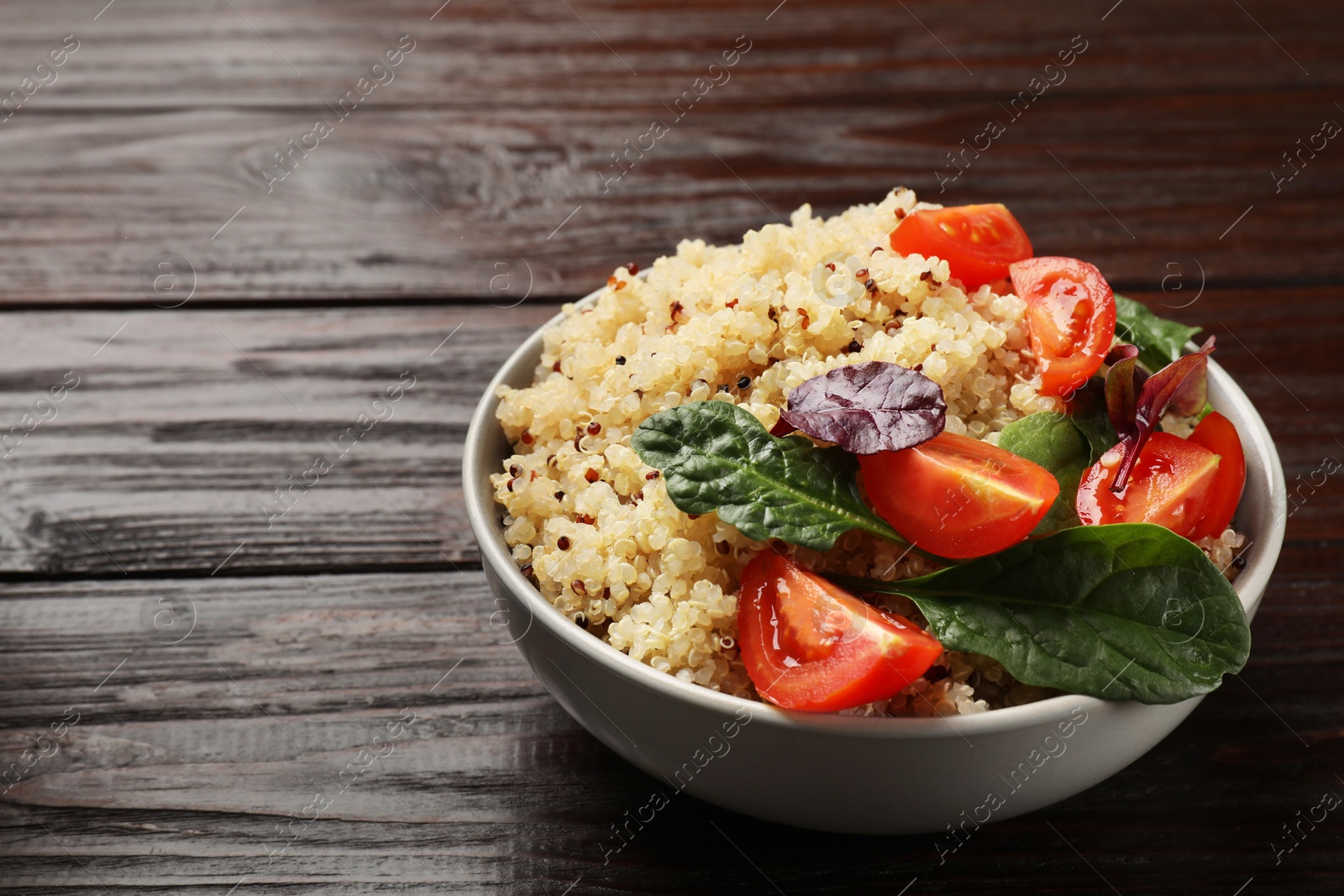 Photo of Tasty quinoa porridge with tomatoes and spinach in bowl on wooden table, closeup. Space for text