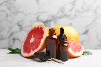 Bottles of essential oil and grapefruits on table against marble background