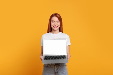 Photo of Smiling young woman showing laptop on yellow background