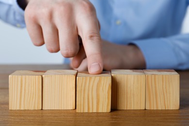 Photo of Man arranging empty cubes in row on wooden table, closeup. Space for text