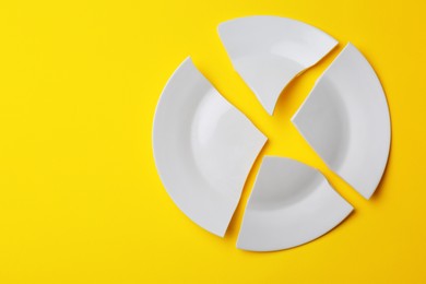 Photo of Pieces of broken white ceramic plate on yellow background, top view. Space for text