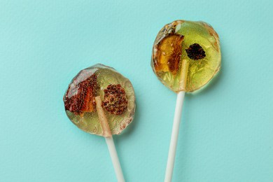 Sweet colorful lollipops with berries on turquoise background, flat lay