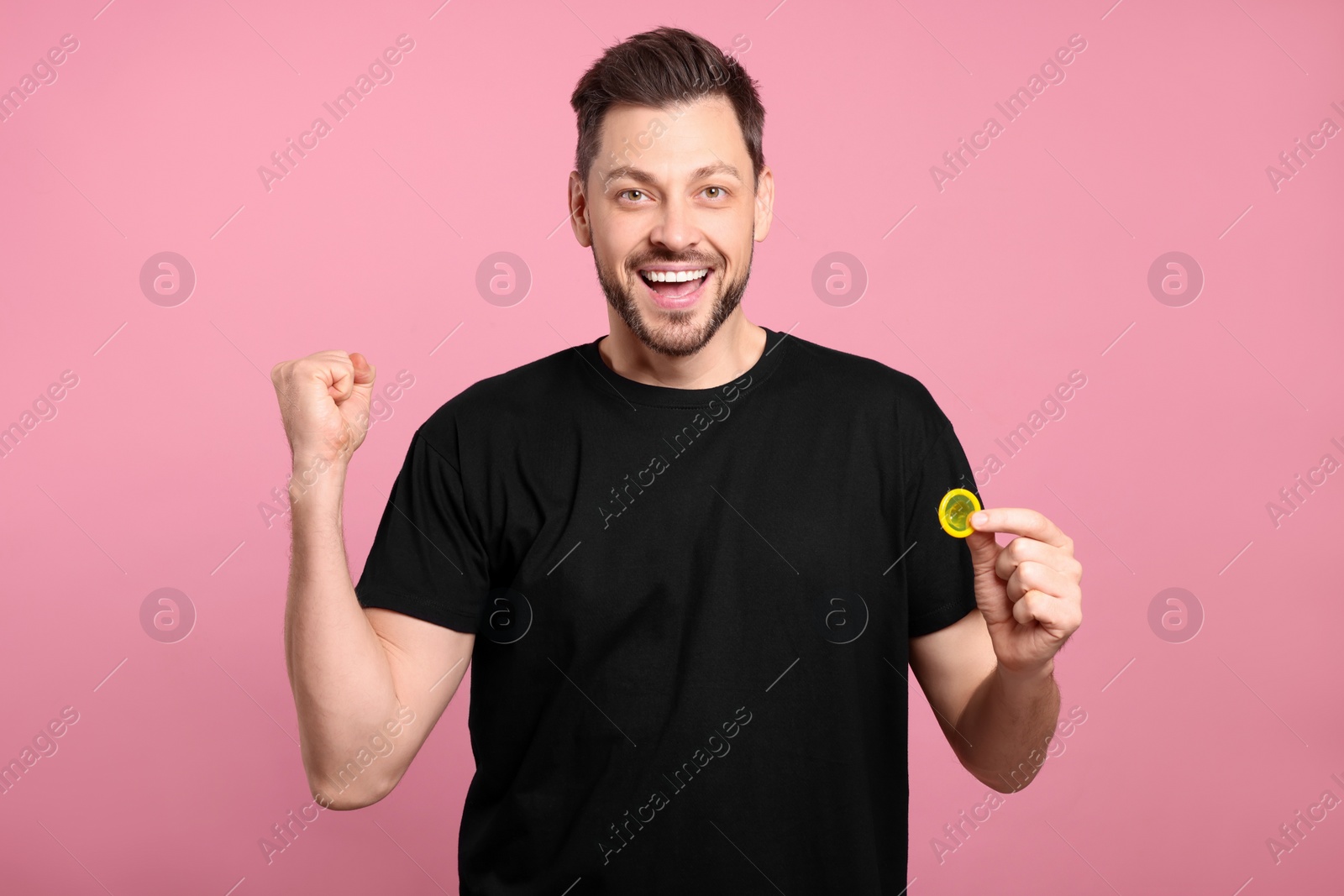 Photo of Excited man holding condom on pink background