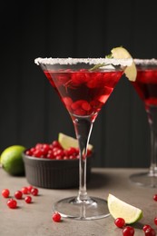 Tasty cranberry cocktail with rosemary and lime in glass on grey table against black background