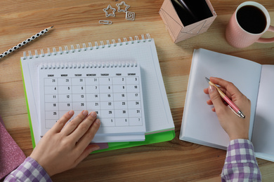 Photo of Woman making schedule using calendar at wooden table, top view