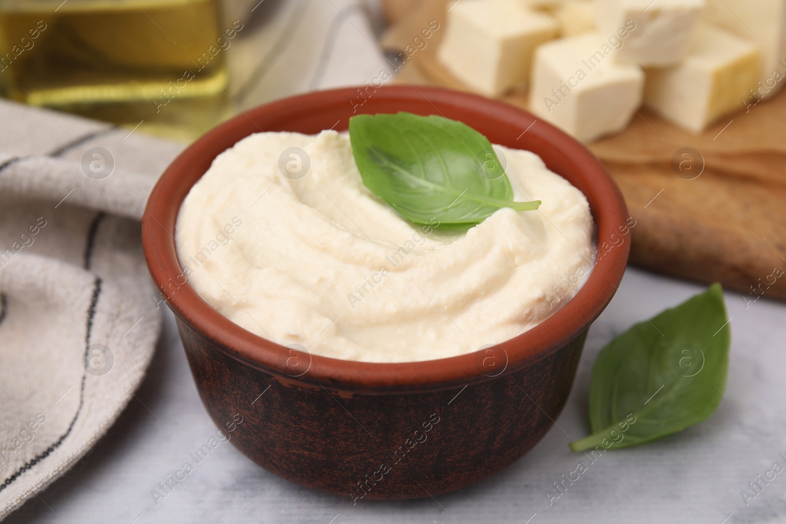 Photo of Delicious tofu sauce and basil leaves on white table, closeup