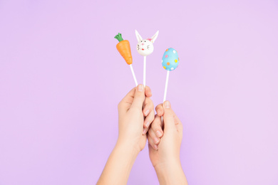 Photo of Woman with delicious cake pops on light pink background, closeup. Easter holiday