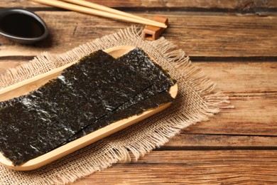 Dry nori sheets, soy sauce and chopsticks on wooden table