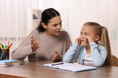 Dyslexia problem. Annoyed mother helping daughter with homework at table in room