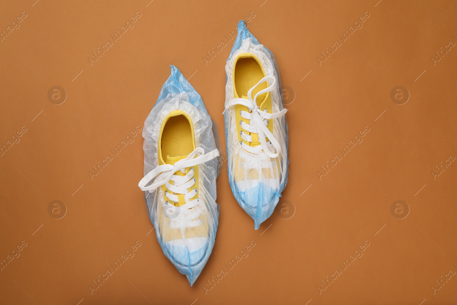 Photo of Sneakers in shoe covers on brown background, top view