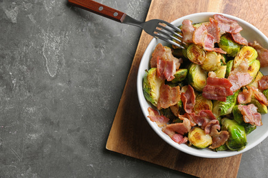 Photo of Delicious roasted Brussels sprouts with bacon served on grey table, flat lay. Space for text