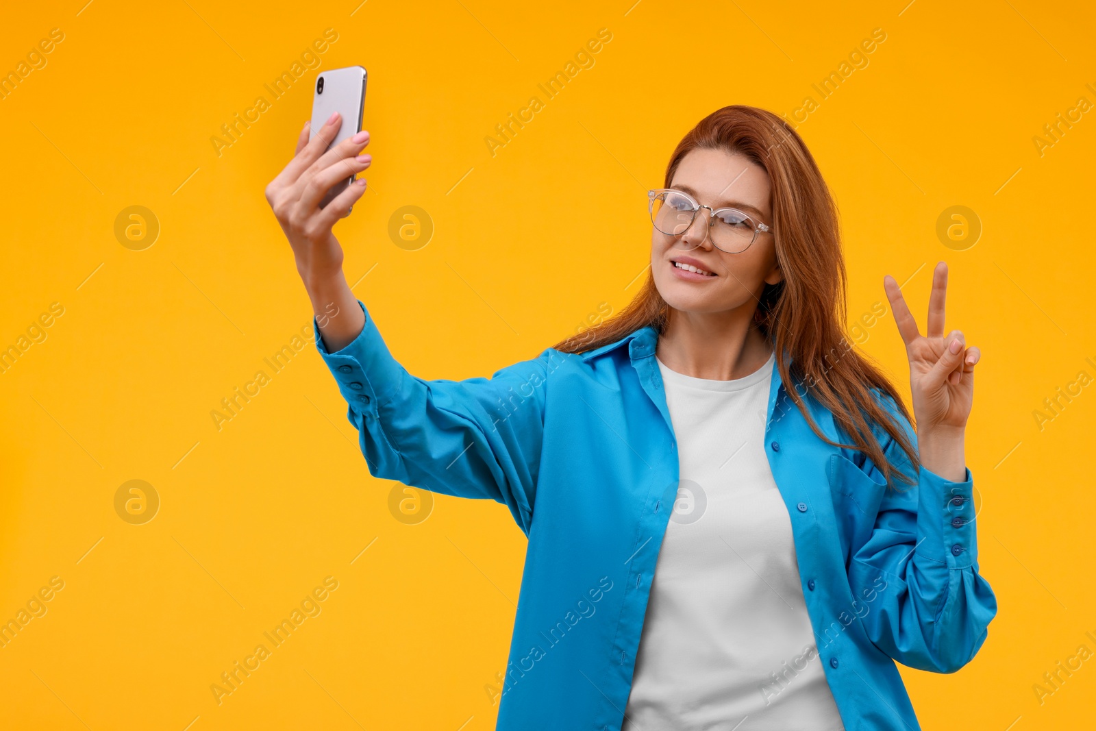 Photo of Beautiful woman in eyeglasses taking selfie on orange background