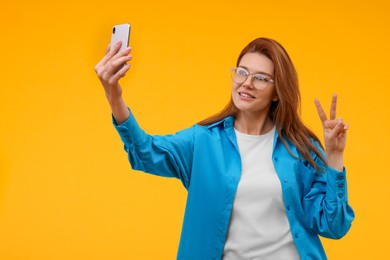 Beautiful woman in eyeglasses taking selfie on orange background