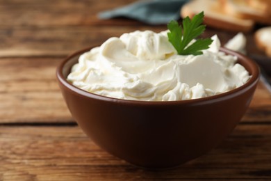 Photo of Bowl of tasty cream cheese and parsley on wooden table, closeup