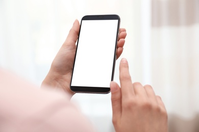 Woman holding smartphone with blank screen on blurred background, closeup of hands. Space for text