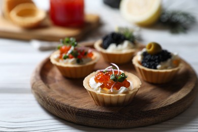 Delicious tartlets with red and black caviar served on white wooden table, closeup