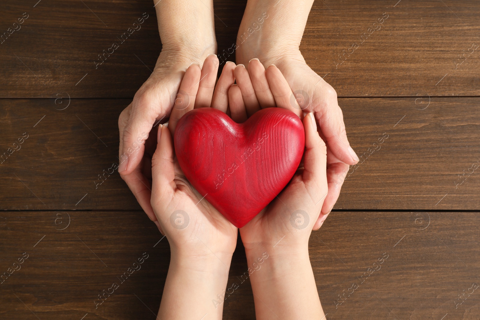 Photo of Young and elderly women holding red heart at wooden table, top view