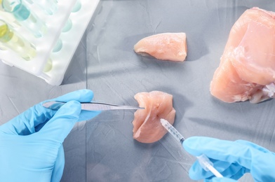 Scientist injecting liquid into meat sample on table, top view. Food quality control