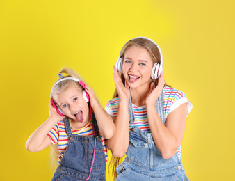 Photo of Happy mother and little daughter with headphones on yellow background