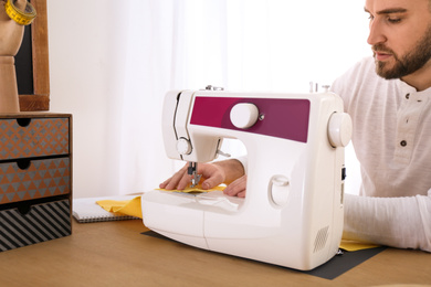 Fashion designer sewing new clothes with machine in studio, closeup