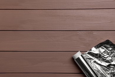 Photo of Roll of aluminum foil on wooden table, top view. Space for text