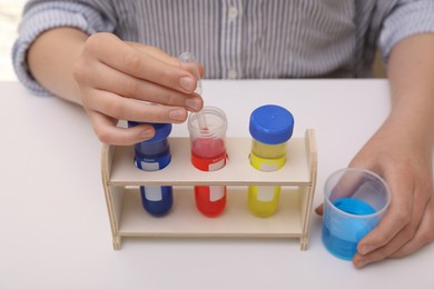 Photo of Girl with colorful liquids in test tubes and beaker at white table indoors, closeup. Chemical experiment set for kids
