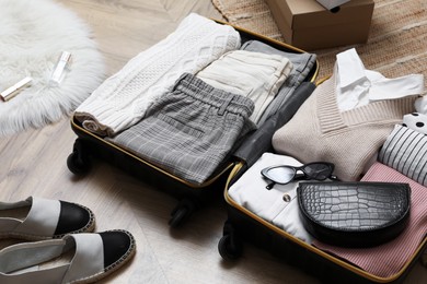 Photo of Open suitcase with folded clothes, accessories and shoes on floor