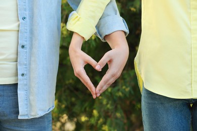 Photo of Couple making heart with hands outdoors on sunny day, closeup