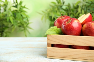 Photo of Wooden crate with ripe juicy red apples on white table against blurred background. Space for text