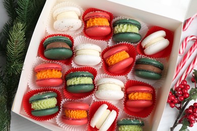 Photo of Different tasty Christmas macarons in box and festive decor on white table, flat lay