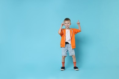 Photo of Happy little boy dancing on light blue background. Space for text