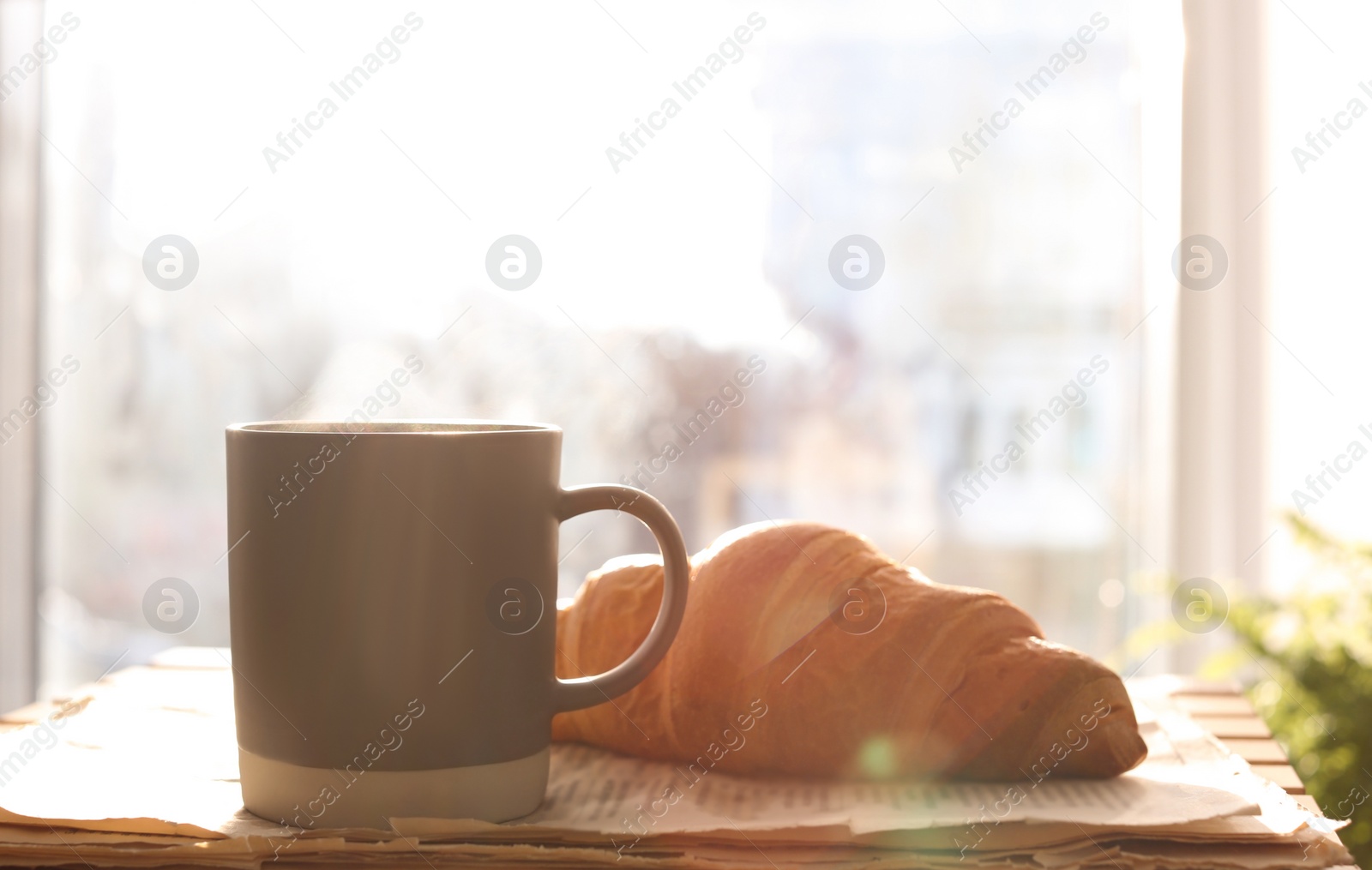 Photo of Delicious morning coffee, newspaper and croissant near window indoors