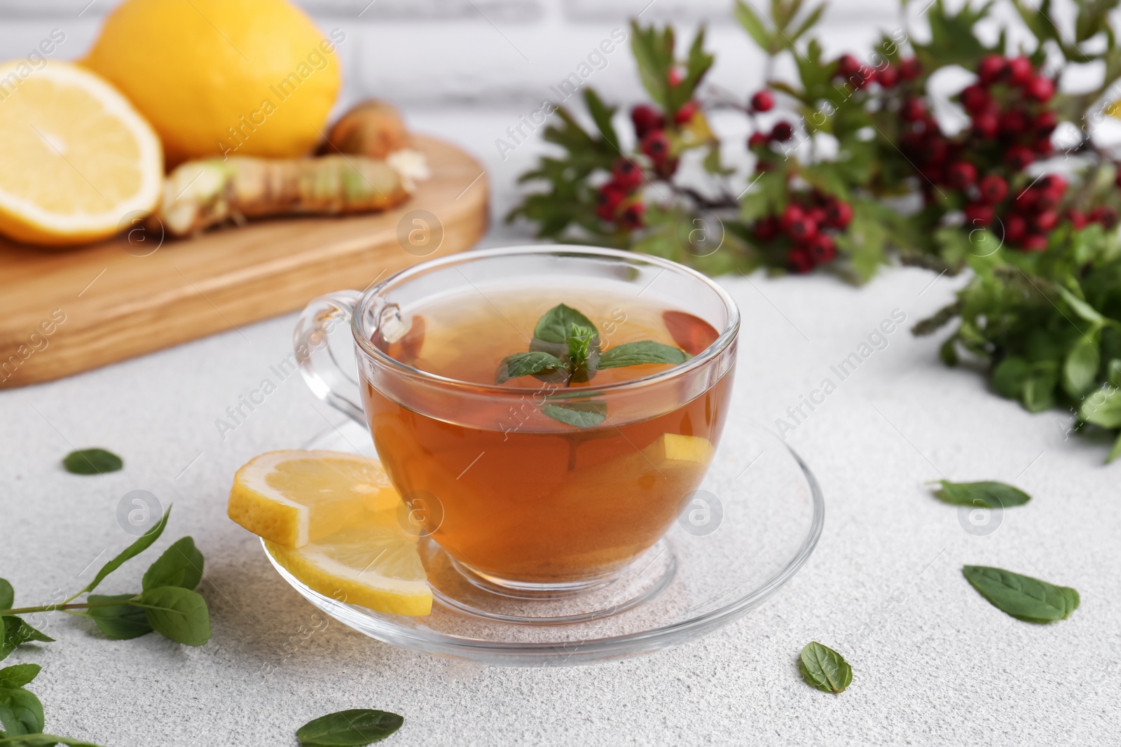 Photo of Glass cup of delicious immunity boosting tea with ingredients on light grey table