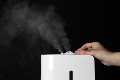 Woman using modern air humidifier on black background, closeup