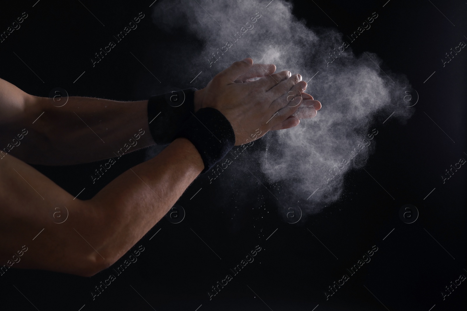 Photo of Young man applying chalk powder on hands against dark background