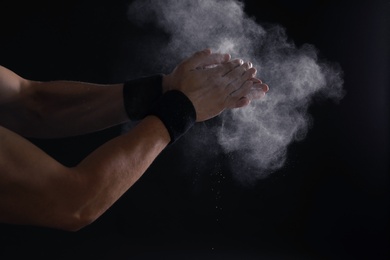 Young man applying chalk powder on hands against dark background