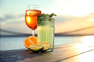 Glasses of fresh summer cocktails on wooden table outdoors at sunset. Space for text