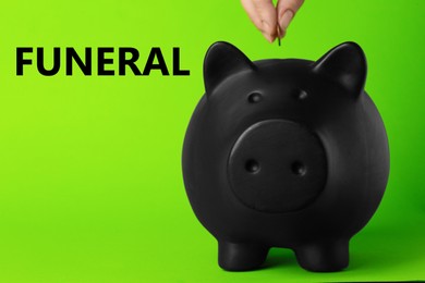 Money for funeral expenses. Woman putting coin into black piggy bank on green background, closeup